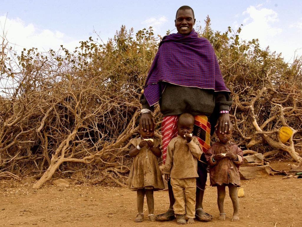 man in purple hoodie standing beside brown bare tree during daytime
